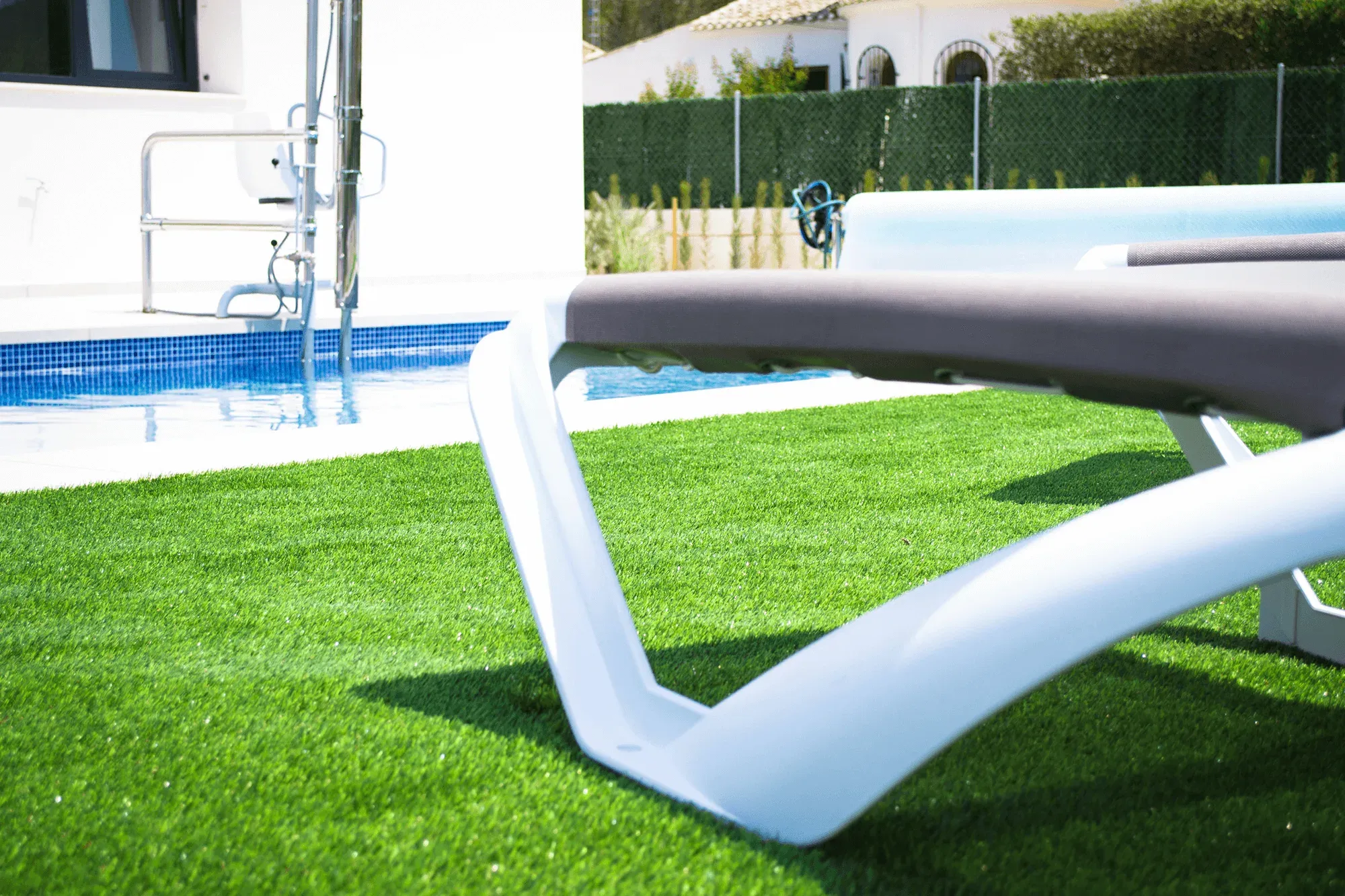 A sun lounger on the lawn beside the pool, with the pool hoist at the water's edge